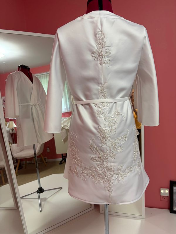 The back of a short white robe with lace appliqué, on a dress form