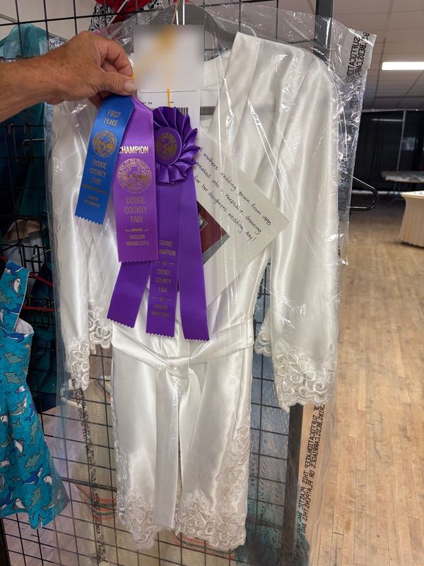A satin robe with lace cuffs hanging at the Dodge County Fair with First Place, Champion and Grand Champion ribbons